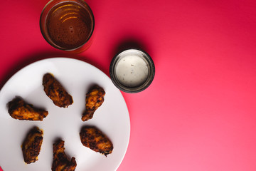 Chicken wings, dipping sauce and beer on pink background.