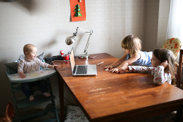 baby in highchair and two sisters watch on laptop