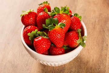 several strawberries in a white pot on a wooden table