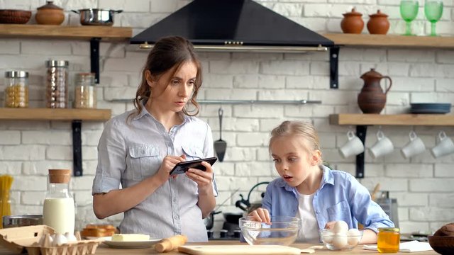 Mother and daughter cheking recipe and list of ingredients. Daughter looking for flour.