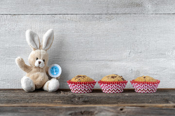 Stoffosterhase mit drei Muffins vor Holzwand