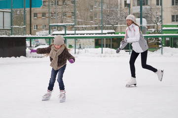 Happy mother and daughter skating on a outdoor skating rink