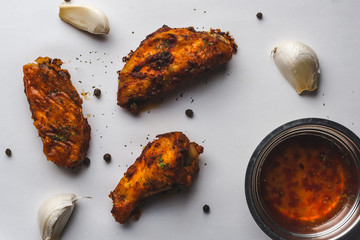 Chicken wings, garlic, pepper corns and spices with chili sauce on white background.
