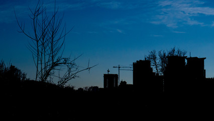 Silhouette of buildings and tower cranes against a blue sky