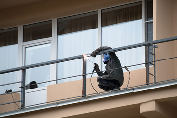 Male worker welds metal railing on the balcony of the building