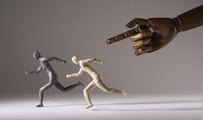 Men run under the threat of a giant hand. Isolated on gray background. With copy space text. Studio Shot.