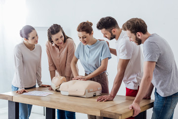 group of smiling people performing cpr on dummy during first aid training