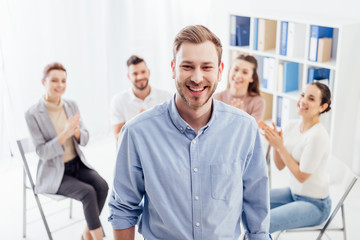 smiling man looking at camera while people sitting during group therapy session