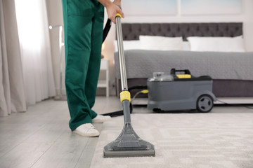 Professional janitor removing dirt from carpet with vacuum cleaner in bedroom, closeup. Space for text