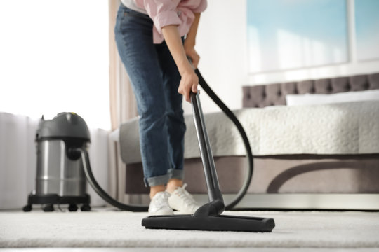 Woman removing dirt from carpet with vacuum cleaner at home, closeup