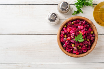 Traditional russian salad vinaigrette with boiled vegetables, pickled cucumbers and sauerkraut in bowl on white wooden table. Top view. Copy space.