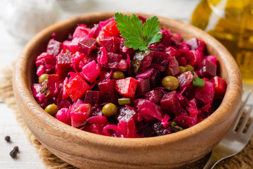 Traditional russian salad vinaigrette with boiled vegetables, pickled cucumbers and sauerkraut in bowl on white wooden table. Selective focus.