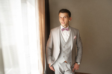 The fashionable bridegroom expects the bride near the window. Portrait of the groom in a grey vest