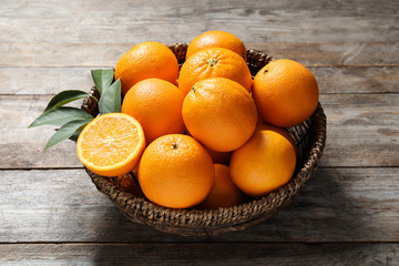 Wicker bowl with ripe oranges on wooden background