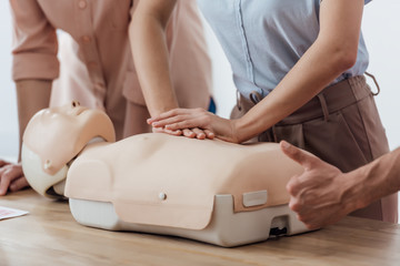 cropped view of woman performing chest compression on dummy during cpr training class while man doing thumb up sign
