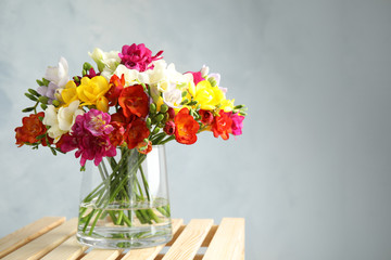 Bouquet of spring freesia flowers in vase on color background. Space for text