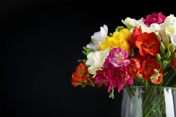 Bouquet of spring freesia flowers in vase on dark background, closeup. Space for text