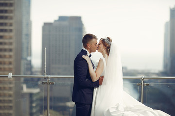 Elegant bride in a white dress and veil. Handsome groom in a blue suit. Couple in a big town