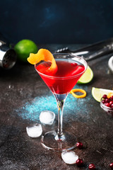 Classic alcoholic cocktail cosmopolitan with vodka, liqueur, cranberry juice, lime, ice and orange zest, dark bar counter background, night mood, space for text