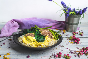 in a bright, rustic kitchen, on a wooden table lies a plate of spaghetti with cheese sauce, garlic, meatballs, spinach and green bean stew