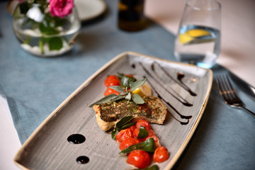fried piece of fish with tomato and lemon on a plate