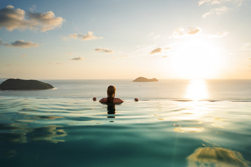 Fototapeta premium girl in the pool at sunset with views of the mountains and the sea