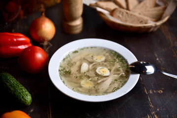 chicken soup with quail eggs in a white plate on a wooden background