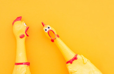 Surprised chicken toys are isolated on a orange background, one looks at the camera and shouts, the other one to the side. Screaming chicken toys on a yellow background.