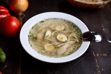 chicken soup with quail eggs in a white plate on a wooden background