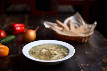 chicken soup with quail eggs in a white plate on a wooden background
