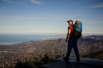 Strong man with a backpack standing and looking on the mountains