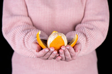 Peeled orange on the palms of a girl in a pink sweater.