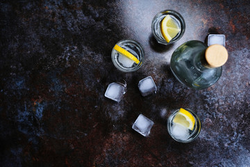 Cold vodka in shot glasses with lemon on stone background. Top view, copy space.