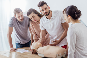 man holding cpr dummy and looking at camera during first aid training class with group of people