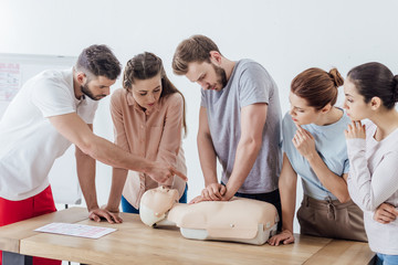 group of people with instructor performing cpr on dummy during first aid training