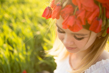 Portrait of a beautiful girl in a wreath of red poppies on a summer field 