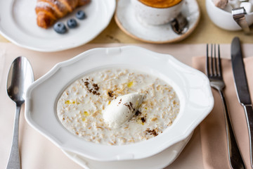 Bowl of breakfast oatmeal with soft Italian cheese and cinnamon. Croissants, coffee and other dishes on the table in the restaurant