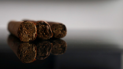 Tree Cuban cigars on a black glass table 
