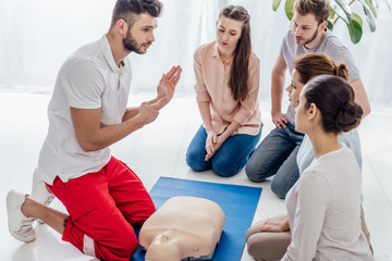 handsome instructor gesturing during first aid training with group of people