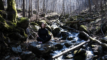 young Fitnest girl making Yoga Pose lotus Sitting in a rock on a river Meditating in the forest with sunlight