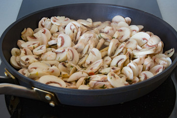 Champignon mushrooms are fried in a frying pan