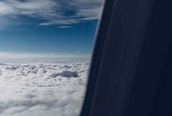 Airplane window view over horizon covered by white clouds beneath sunny blue sky.