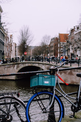 Stylish oldschool bike with red ribbon and blue basket near a bridge over a canal in Amsterdam. Charming dreamy cityscape. Cold and rainy weather in the capital of Netherland