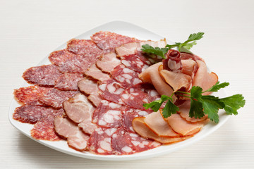 There is a variety of sausages and prosciutto on the plate, the meat assortment is decorated
