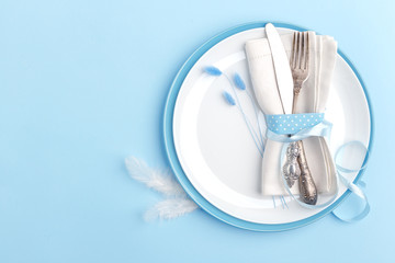 Elegant stylish table setting. Knife and fork on a napkin on a plate on a blue background.