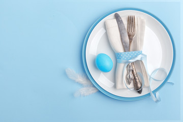 Elegant stylish table setting. Knife and fork on a napkin on a plate on a blue background.