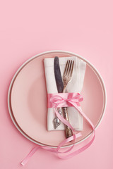 Elegant stylish table setting. Knife and fork on a napkin on a plate on a pink background.