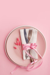 Elegant stylish table setting. Knife and fork on a napkin on a plate on a pink background.