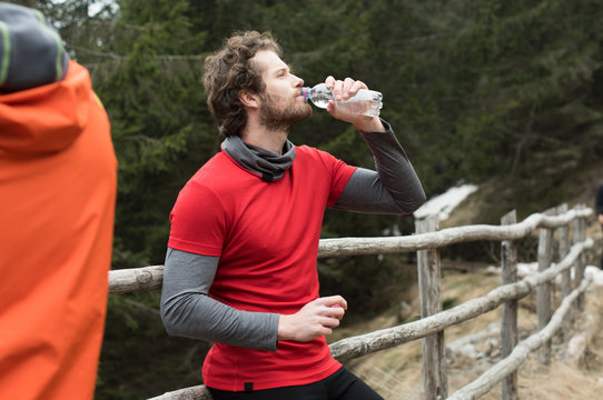 Man drinking water while leaning against fence
