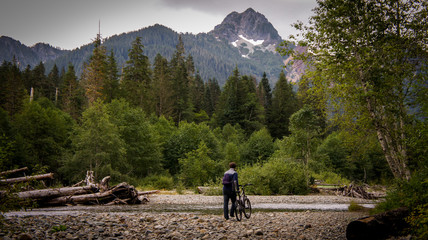 Man walks his bike over rocks towards a mountain.